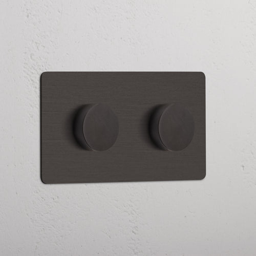 Bronze Double 2x Multiway Dimmer Switch with two round knobs, installed on a white textured wall.