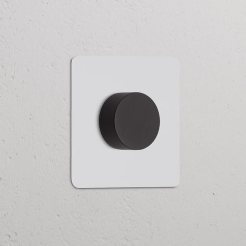 Single Multiway Dimmer Switch in paintable bronze finish with central knob, shown on a white wall.